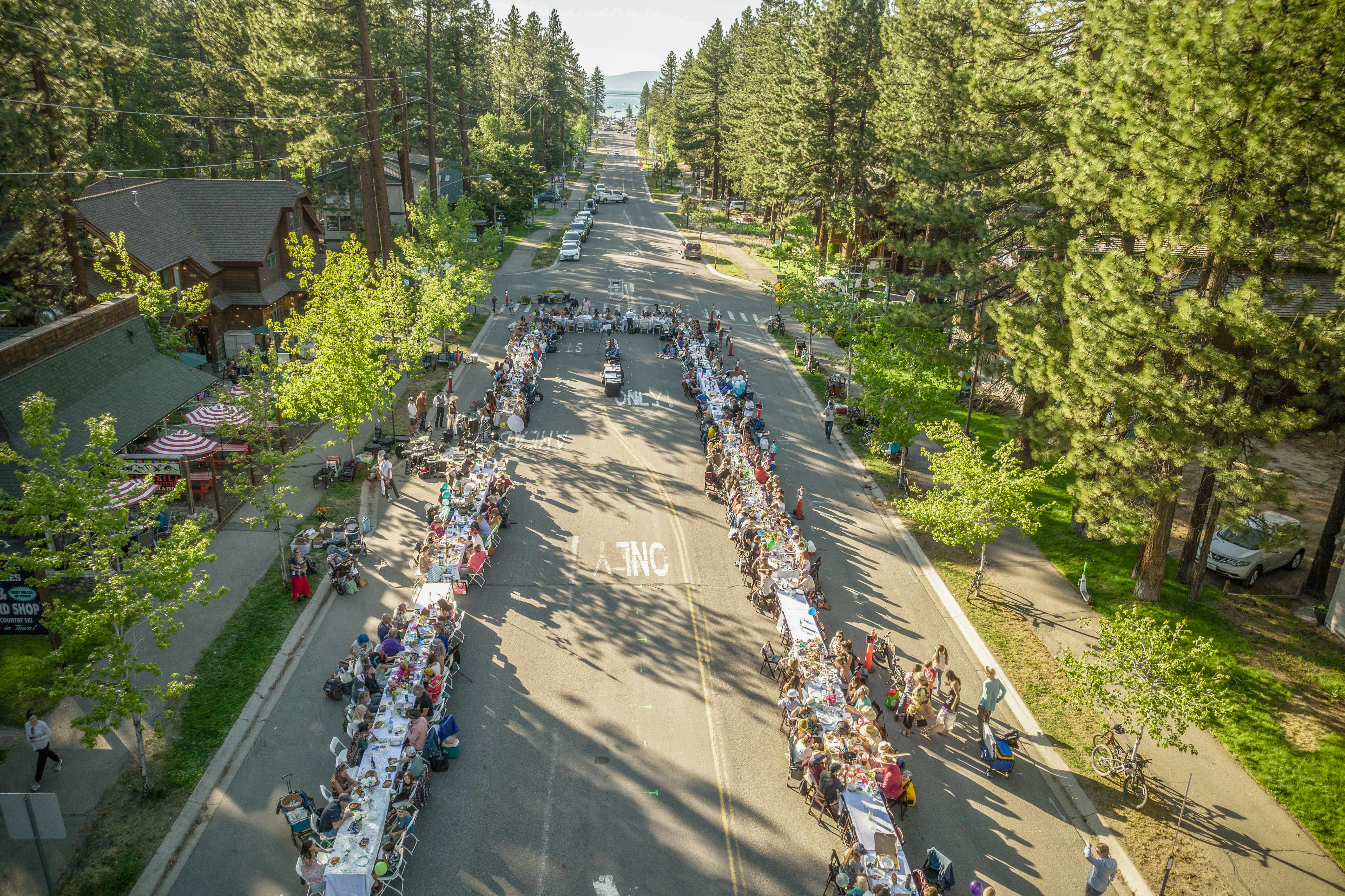 Aerial drone shot of The Longest Dinner Table stretching down Ski Run Blvd through the pines toward Lake Tahoe